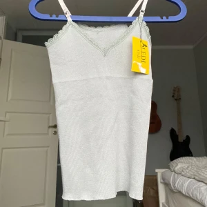 Grått linne med spets - Säljer ett sött grått linne i storlek XS.  Toppen har spetsdetaljer vid halsringningen och smala axelband. Helt ny med tag kvar!