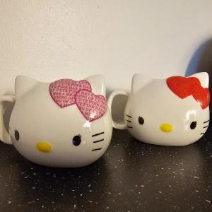 Hello Kitty 35-årsjubileumsmuggar - Två supergulliga Hello Kitty-muggar i keramik, designade för 35-årsjubileet. En mugg har en röd rosett och den andra en rosa med text. Perfekta för samlare eller som en söt present! 🐱🎀