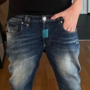 Blå jeans från Philipp Plein - Säljer ett par snygga blå jeans från Philipp Plein. De har en cool slitning och en logga på bakfickan. Perfekta för en casual look eller en utekväll. Midjan är normal och passformen är slim fit, vilket gör dem bekväma att bära hela dagen. Storlek w 30 ny pris ca 6000kr köpts på whallenbergs kan eventuellt gå ner i pris vid snabb affär