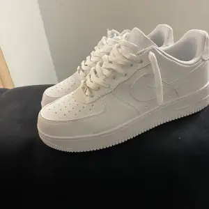 Säljer ett par klassiska vita Nike Air Force sneakers i nytt skick. De har en stilren design med snörning och perforerade detaljer för extra ventilation. Perfekta för både vardag och fest! 🏀👟