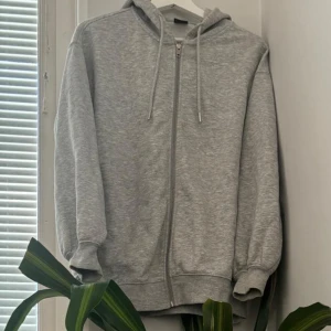 Grå hoodie från Gina Tricot - Mysig grå hoodie från Gina Tricot i storlek XS men skulle säga mer M i storlek. Perfekt för kyliga dagar med dragkedja och justerbar huva. Den är i bra skick och passar till vardags eller en avslappnad dag hemma. Den har knappt använts så är i nytt skick.
