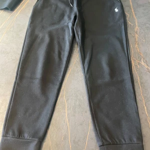 Svarta mjukisbyxor från Polo Ralph Lauren - Säljer ett par svarta mjukisbyxor från Polo Ralph Lauren i storlek L (Funkar som M) Byxorna har en klassisk design med elastiska muddar vid bensluten och en liten logga på sidan. Perfekta för en avslappnad stil eller mysiga dagar hemma. 🖤