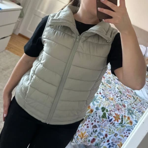 Väst med dragkedja och dragsko i midjan - mycket bra skick då den endast är använd 2 gånger. Västen har en dragkedja framtill samt dragsko nedtill för att justera hur tajt eller löst man vill ha den och kragen går att ha både uppvikt och nervikt beroende på hur man vill ha den. Lite grågrön färg