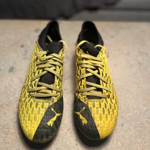 Gula och svarta Puma fotbollsskor - Säljer ett par fotbollsskor från Puma i storlek 38.5. Skorna har en gul och svart design med slitstarka dobbar och meshliknande ovandel för ökad ventilation. Passar perfekt för spel på gräsplaner.  Skick: Skorna är ok skick men har några märken av slitage på dobbar och ovandel. Fullt funktionella . 