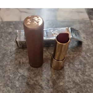 Läppstift från Lancôme - Elegant läppstift från Lancôme i nyansen 'Burning Lips 155'. Hylsan är i en lyxig guld- och bronsfärg med en vacker logotyp på toppen. Perfekt för att ge dina läppar en djup och intensiv färg. 
