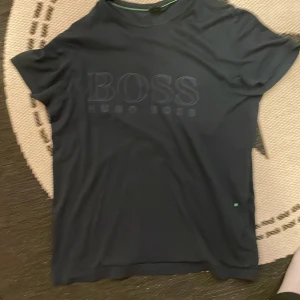 Svart t-shirt från Hugo Boss - Snygg svart t-shirt från Hugo Boss med diskret logga på bröstet. Perfekt för en stilren look. Kortärmad och tillverkad i mjukt material för extra komfort.