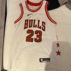 Vit basket tröja från nike  - Säljer en vit basketlinne från Nike med röd och svart text. Den har nummer 23 och namnet Jordan på ryggen. Linnet har röda stjärnor på sidan och är ärmlöst med en rund halsringning.