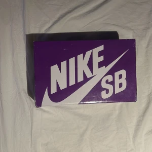 Nike SB Dunk sneakers - Säljer ett par Nike SB Dunk sneakers i grå och svart med vit sula. Skorna har en hög modell med snörning och extra skosnören i vitt och blått. Perfekta för skate eller vardagsbruk.