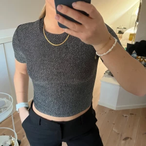 Svart glittrig croppad topp från Bik Bok - Snygg svart glittrig croppad topp från Bik Bok. Den har korta ärmar och en tight passform! Storlek XS