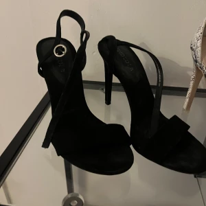 Svarta klackskor med remmar - Eleganta svarta klackskor med smala remmar och öppen tå. Perfekta för en stilren look.