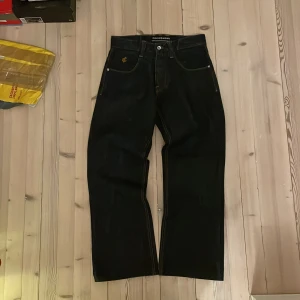 Svarta jeans från Rocawear - Snygga svarta jeans från Rocawear med broderade detaljer på bakfickorna i färgglada nyanser. Jeansen har en klassisk femficksdesign och en rak passform. Perfekta för en stilren look.