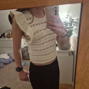 Beige stickad topp från H&M - Säljer en söt beige stickad topp från H&M med volangdetaljer på axlarna. Toppen är ärmlös och har ett fint hålmönster som ger en luftig känsla. Perfekt för varmare dagar!