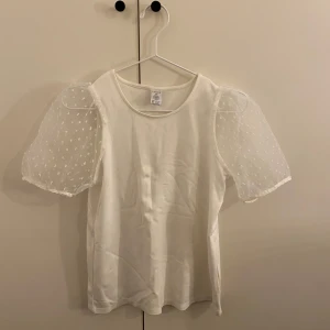 Vit blus med puffärmar - Säljer en söt vit blus med transparenta puffärmar och små prickar. Perfekt för en stilren och elegant look. Blusen har en rund halsringning och normal passform.