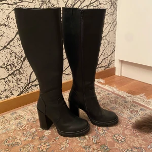 Svarta höga stövlar med klack - Snygga svarta stövlar i skinn med hög klack och dragkedja på sidan. Perfekta för höst och vinter. Endast använda 2 gånger men har fått märken, dessa syns knappt från långt håll då de är så svarta. Priset kan alltid diskuteras