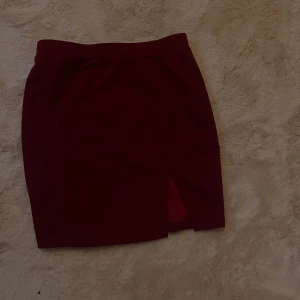 Vinröd kjol med slits - Snygg vinröd kjol med en stilren slits framtill. Perfekt för att ge en elegant touch till din outfit. Kjolen har en enkel design som gör den lätt att matcha med olika toppar.