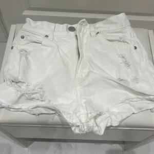 Vita jeansshorts med slitningar - Snygga vita jeansshorts med slitna detaljer och råa kanter. De har en dragkedja och knapp framtill samt fickor både fram och bak. Perfekta för en avslappnad sommarlook.