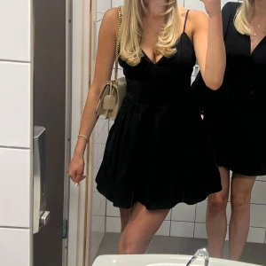 Svart klänning med spetsdetaljer - Elegant svart klänning med smala axelband och spetsdetaljer vid halsringningen. Klänningen har en v-ringad design och en kort längd som ger en stilren look. Perfekt för en kväll ute eller mösspåtagning 🥰