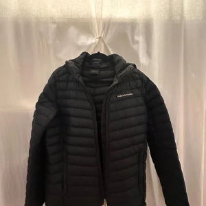 Svart dunjacka från Peak Performance - Snygg svart dunjacka från Peak Performance med dragkedja och hög krage. Perfekt för kyliga dagar med sin quiltade design och stilrena look. Jackan har en diskret logga på bröstet och ärmarna. Pris kan diskuteras men KÖPAREN STÅR GÖR FRAKT 📦 