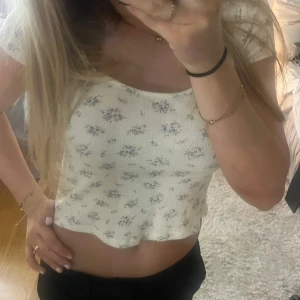 Blommig croppad topp - Söt blommig croppad topp i vitt. Toppen har korta ärmar och en rundad halslinje. Perfekt för en avslappnad sommarlook.🩷