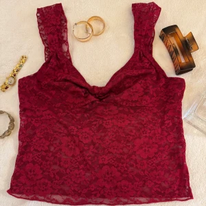 Vinröd spetslinne - Snygg vinröd spetslinne med breda axelband och blommigt mönster. Perfekt för en kväll ute eller en speciell tillställning. Linnet har en elegant och feminin design.