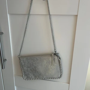 Silverfärgad axelväska med kedjedetaljer - Säljer denna fina  silvriga väska som passar till de nästa💕