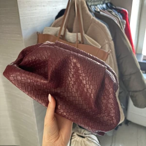 Vinröd kuvertväska i syntet - Snygg vinröd kuvertväska med ett trendigt ormskinnsmönster. Perfekt för att ge en touch av stil till din outfit. Väskan är kompakt och lätt att bära med sig. Knappt använd! 