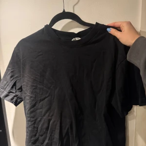 Svart t-shirt från Gina Tricot - Säljer en klassisk svart t-shirt från Gina Tricot. Den har en rund halsringning och korta ärmar, perfekt för en enkel och stilren look. Passar till det mesta och är ett måste i garderoben.
