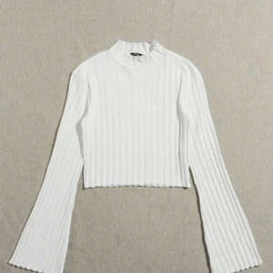 Vit ribbad polotopp - Snygg vit ribbad polotopp med långa ärmar. Perfekt för en stilren look och kan matchas med olika outfits. Den croppade designen ger en modern touch.