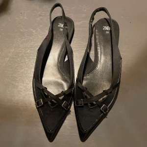 Svarta ballerinaskor med spetsig tå - Eleganta svarta ballerinaskor från Zara med spetsig tå och dekorativa remmar med små spännen. Perfekta för en stilren look.