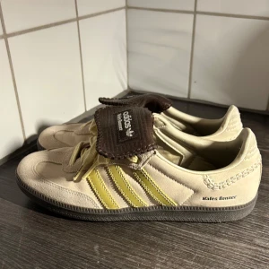 Adidas Wales Bonner sneakers - Snygga Adidas Wales Bonner sneakers i beige med gula detaljer och bruna snörningsflikar. Nästan oanvända Adidas x Wales bonner samba i väldigt bra skick, storlek 41 köpta i New Nork på therealreal (borttappat kvitto). Skollåda, dust bag och extra skosnöre tillkommer.