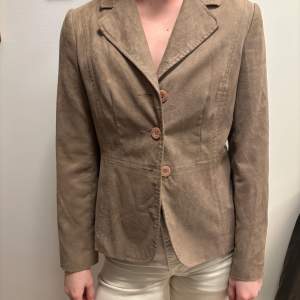 Snygg beige kavaj med två knappar framtill. Tillverkad i ett mjukt material som ger en stilren look. Perfekt för en chic och elegant stil.