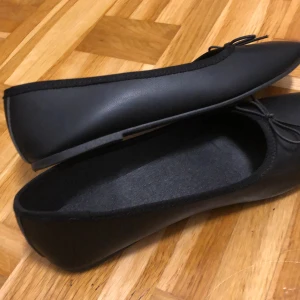 Svarta ballerinaskor från H&M - Snygga svarta ballerinaskor från H&M med en liten rosett framtill. Perfekta för en stilren look och super bekväma att bära hela dagen. Tillverkade i syntetmaterial. 