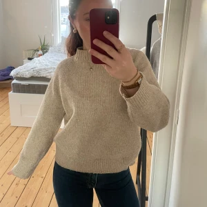 Beige stickad tröja - Säljer en mysig beige stickad tröja med långa ärmar och ribbade muddar. Perfekt för kyliga dagar och enkel att matcha med olika outfits. Tröjan har en klassisk design som passar till många tillfällen.