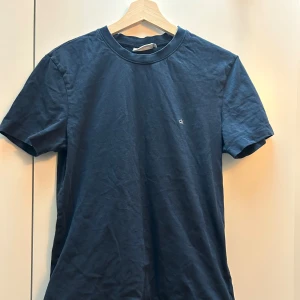 Mörkblå t-shirt från Calvin Klein - Säljer en stilren mörkblå t-shirt från Calvin Klein. Den har en liten logga på bröstet och är tillverkad i mjuk bomull. Perfekt för en avslappnad look.