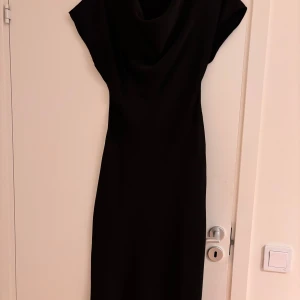 Svart klänning från Neo Noir - Elegant svart klänning från Neo Noir i modellen Lucinda Heavy Sateen. En stilren design med snygg ringning  och korta ärmar. Perfekt för en chic look. Använd en gång. Storlek XS men stor i storleken 