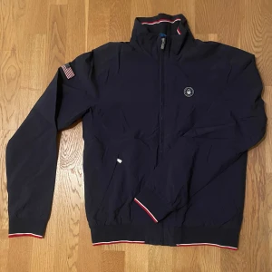 Sail Racing windbreaker - Super schysst vindjacka, perfekt till våren i väldigt bra skick. Storlek small men sitter som en medium. Inga skador i yttertyget eller i fodret. Nypris runt 2000. Hör av er om frågor!