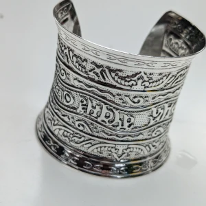 Bred silverfärgad armring med detaljerat mönster - Säljer en supercool bred armring i silverfärg med ett detaljerat och intrikat mönster. Den har en öppen design som gör den lätt att ta på och av. Perfekt för att ge din outfit en unik touch!