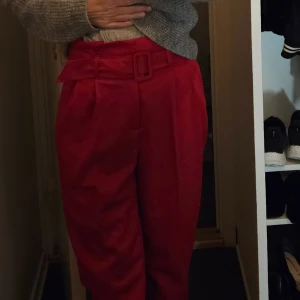 Högmidjade kostymbyxor med bälte nytt - Oanvända Säljer ett par snygga röda kostymbyxor med hög midja och ett matchande bälte. Byxorna har en loose passform och är perfekta för både vardag och fest. De är gjorda i ett mjukt material som känns bekvämt hela dagen.