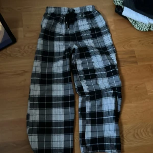 Svart och vit rutiga mjukisbyxor - Säljer ett par superbekväma mjukisbyxor i svart och vit rutigt mönster. De har en elastisk midja med snörning för perfekt passform. Perfekta för en mysig dag hemma eller en avslappnad dag ute.