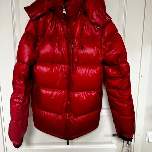 Polo Ralph Lauren Jacka - Säljer en snygg röd dunjacka från Polo Ralph Lauren i mycket bra skick. Storlek är S och passar mellan 173-180cm. Är 175 och passar mig perfekt. Vid minsta lilla fråga tveka inte att fråga. Priset går även att diskutera