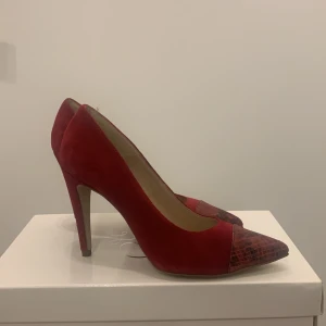 Röda klackskor från 5th Avenue - Snygga röda klackskor i mocka från 5th Avenue. De har en spetsig tå med ett coolt ormskinnsmönster som ger en extra touch. Perfekta för en utekväll eller fest! Skorna är i mycket bra skick och redo att användas. 🍒