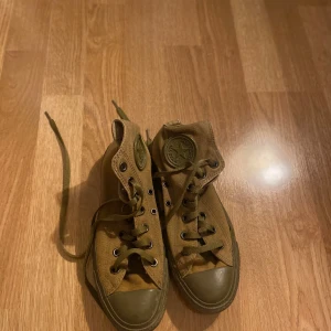 Bruna sneakers med snörning - Säljer ett par militär gröna sneakers i bra skick. De har en klassisk design med snörning och högre skaft. Perfekta för en avslappnad stil och passar till det mesta. Skorna har en robust sula och är bekväma för vardagsbruk.