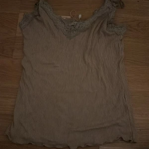 Beige ribbad topp från Amisu - Säljer en söt beige ribbad topp från Amisu i storlek XXS. Toppen har spetsdetaljer vid halsringningen och är perfekt för sommardagar. Den är i ett mjukt och bekvämt material, idealisk för en avslappnad stil.