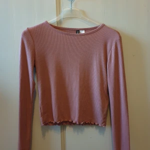 Långärmad croptop - Rosa ribbad långärmad tröja och har en croppad stil med vågig kant nertill. Använd flertal gånger men är fortfarande i bra skick.