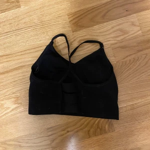 Svart sporttopp från MM Sports - Säljer en svart sporttopp från MM Sports i mycket bra skick. Den har en enkel design med smala axelband och är perfekt för träning. Materialet är stretchigt och bekvämt, vilket gör den idealisk för olika typer av aktiviteter.