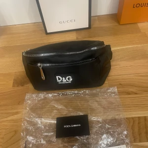 Svart midjeväska från Dolce & Gabbana - Säljer en snygg svart midjeväska från Dolce & Gabbana. Väskan har en praktisk dragkedja och justerbart band. Perfekt för att hålla dina saker säkra och stiliga på språng. Den är i  nytt skick och kommer med originalförpackning.