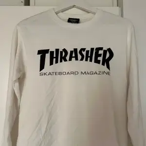 Säljer en vit långärmad tröja från Thrasher med deras ikoniska logga i svart på framsidan. Perfekt för skate-entusiaster eller streetwear-fans. Tröjan är i bra skick och passar perfekt för både vardag och chill. Knappt använd! 