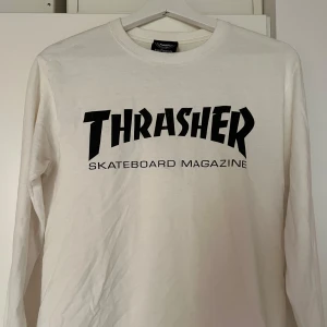Vit långärmad Thrasher-tröja - Säljer en vit långärmad tröja från Thrasher med deras ikoniska logga i svart på framsidan. Perfekt för skate-entusiaster eller streetwear-fans. Tröjan är i bra skick och passar perfekt för både vardag och chill. Knappt använd! 