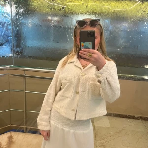 Vit croppad jacka - Säljer en superfin vit croppad jacka med långa ärmar och stora fickor fram. Perfekt för vår och sommar! Den har en stilren look med knappar framtill och är i mycket bra skick. Passar perfekt till både vardag och fest. Den är i storlek M