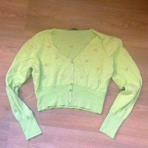 Ljusgrön stickad kofta från BBWM - Säljer en superfin ljusgrön stickad kofta från BBWM. Den har ett sött blommönster i gult och rosa och knappar framtill. Perfekt för vår och sommar! Koftan är croppad och har långa ärmar. Passar perfekt till både jeans och kjol. 🌸